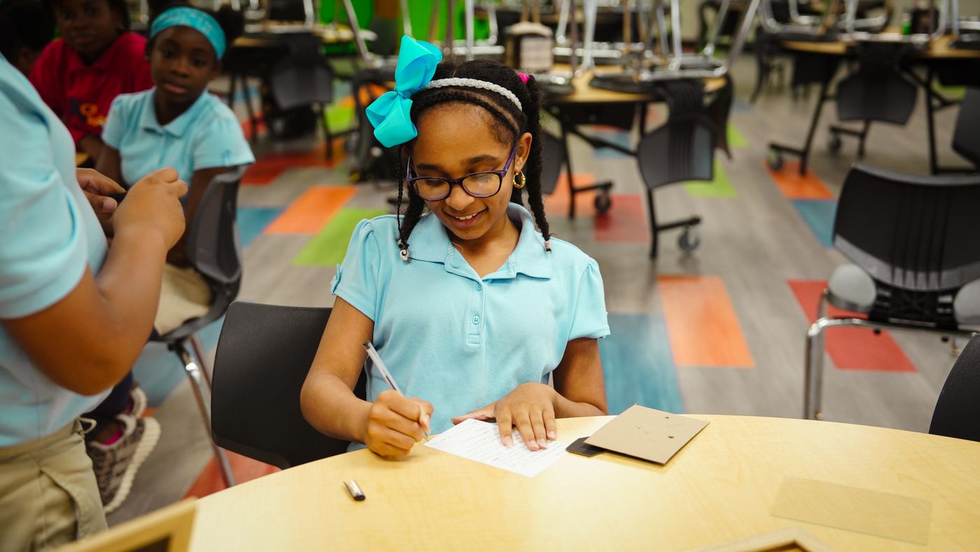 A smiling student writing at a table during the program