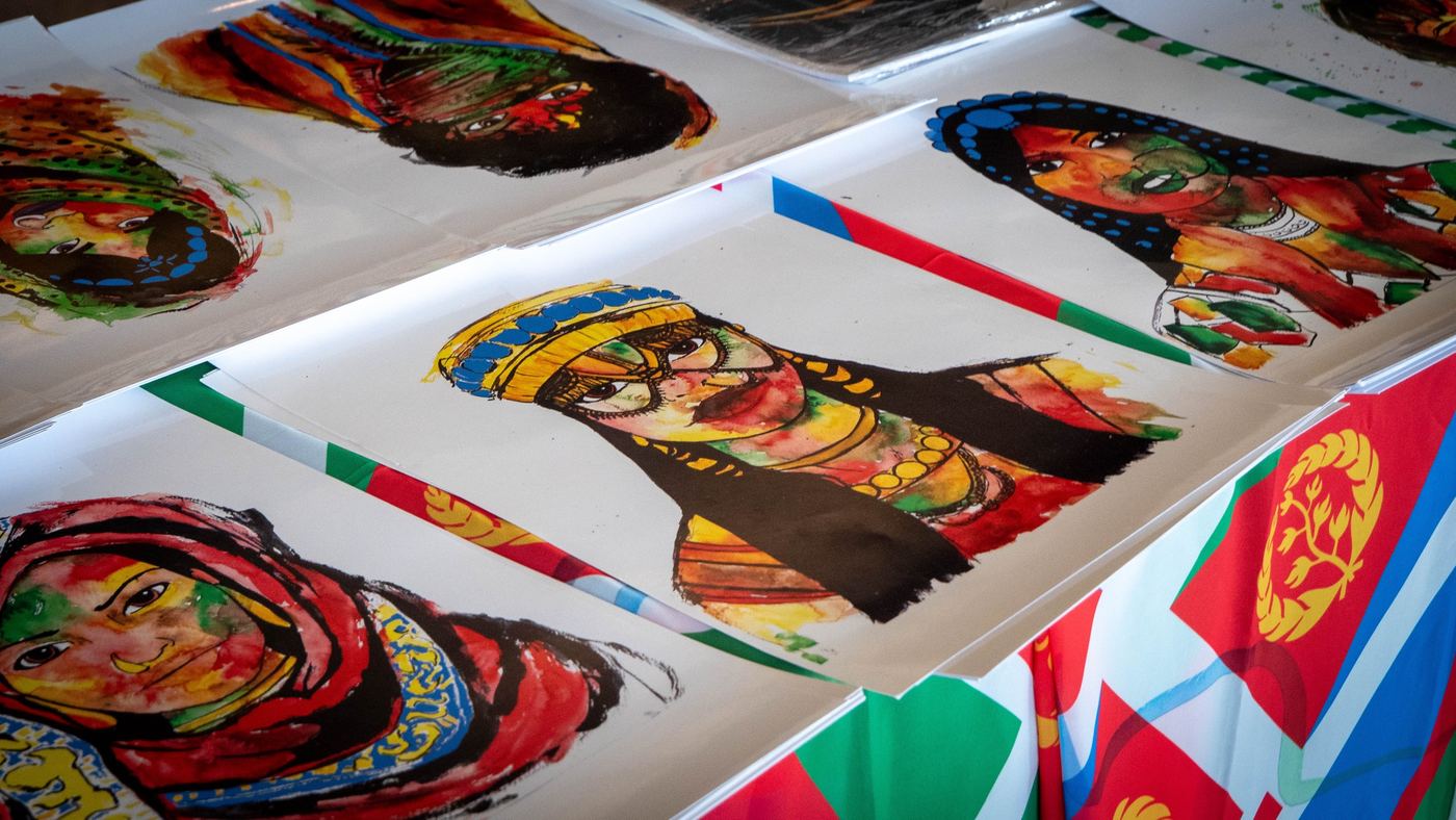 Watercolor portraits of African women displayed on a table draped with flags