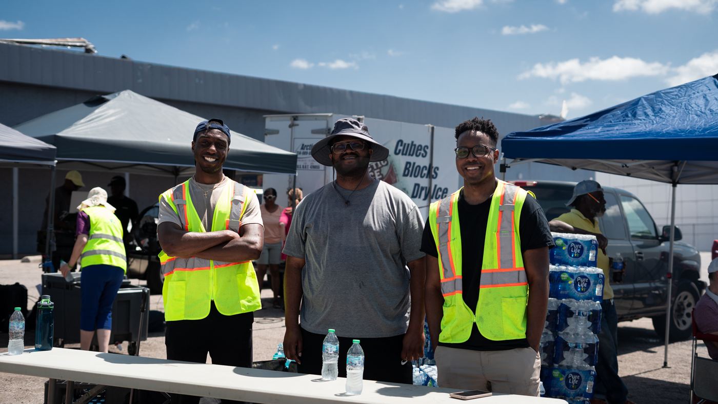 Three volunteers in safety vests smiling at a water station
