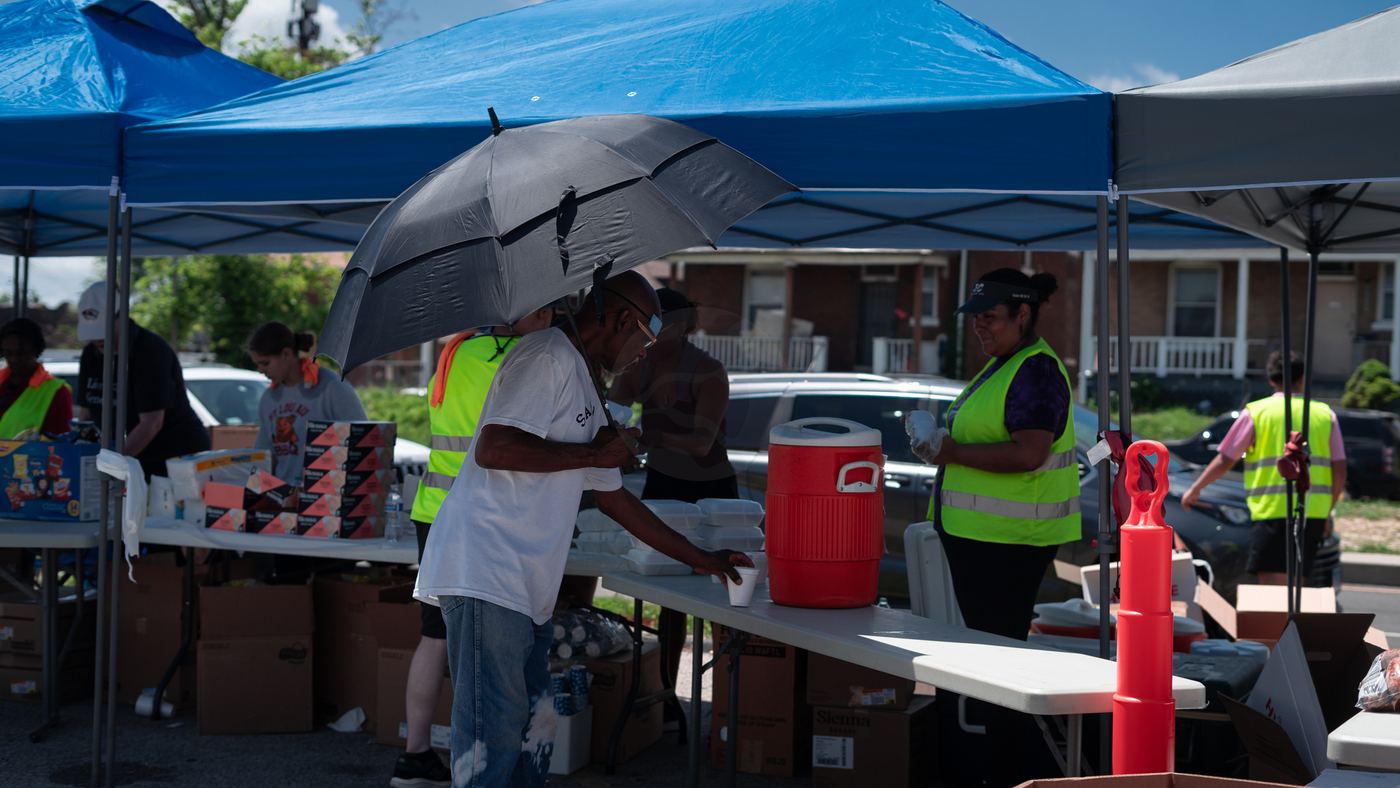 A neighbor under an umbrella getting a cold drink from volunteers